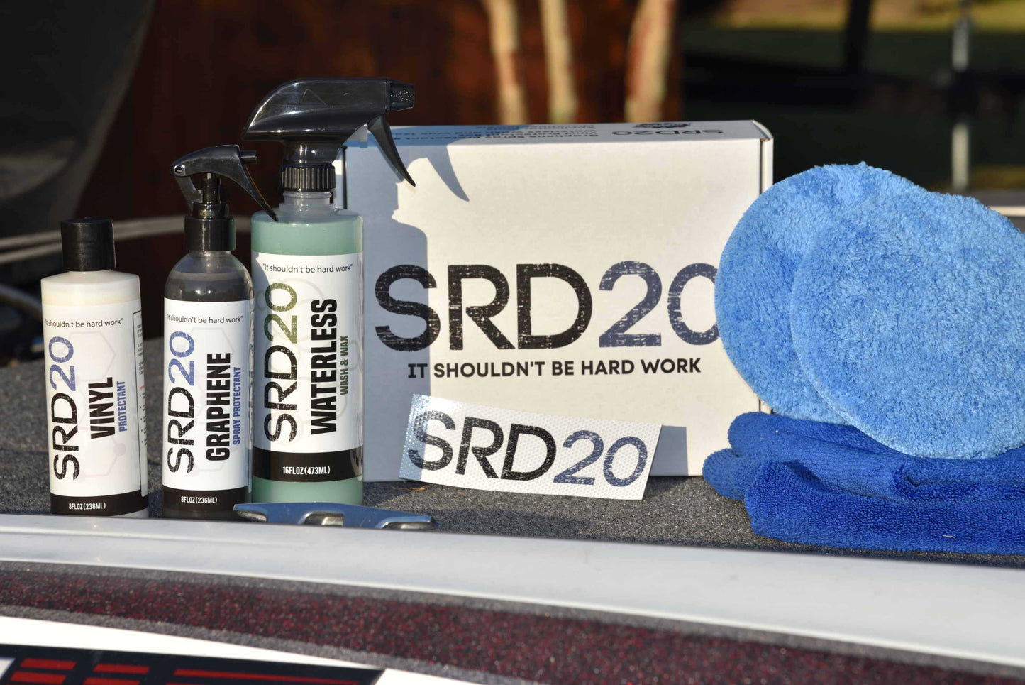 The image shows a set of boat detailing and boat cleaning products from SRD20, including a spray bottle, a wash and wax bottle, a vinyl protectant, two microfiber towels, and a sticker, all displayed on a boat-like surface.